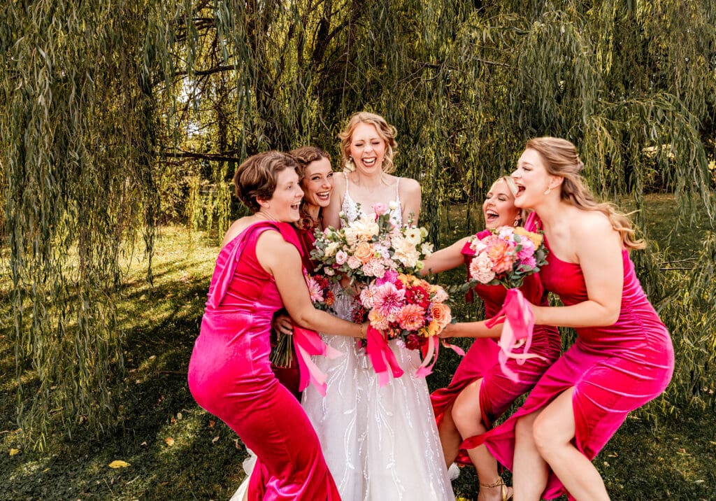 Pittsburgh bridesmaids surrounding and hugging the bride under the willow tree during portraits at The Gathering Place at Darlington Lake