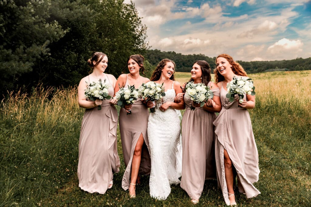 Bride and bridesmaids linking arms and laughing as they walk toward the camera at Sanaview Farm wedding in Somerset, PA