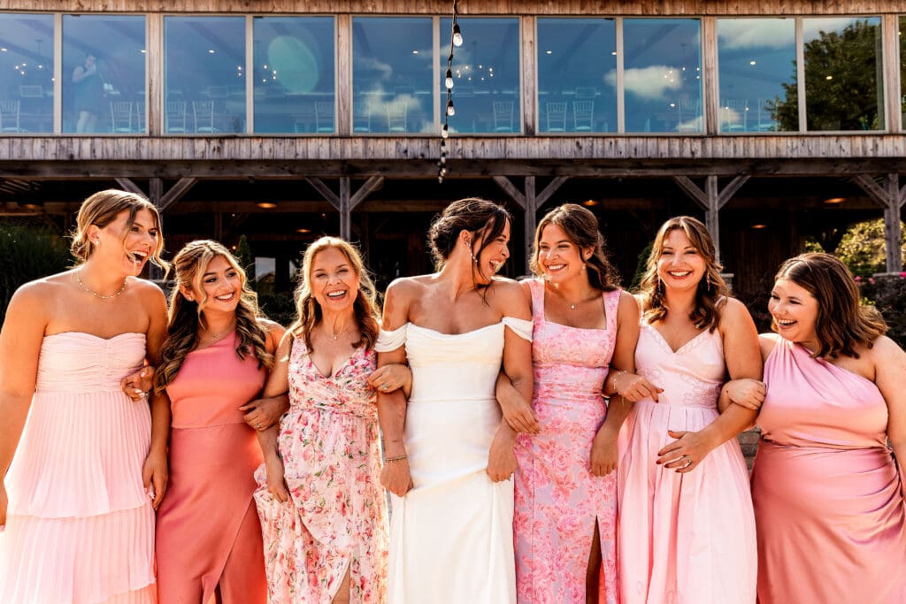 Bride and bridesmaids walking arm in arm and laughing in the courtyard at Willowbrook wedding in Volant, PA