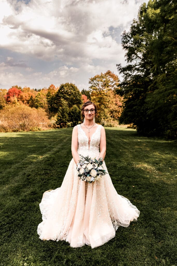 Bride stands in front of fall foliage and pond at Pinehall at Eisler Farm