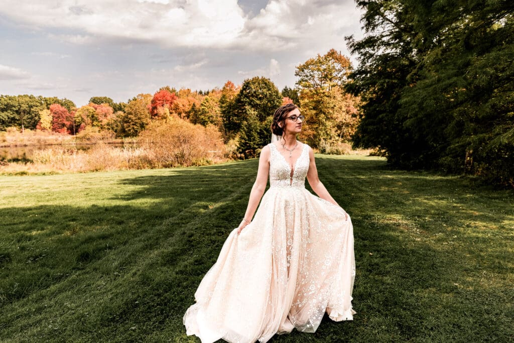 Bride twirling and swishing her dress with fall foliage and pond in the background at Pinehall at Eisler Farm