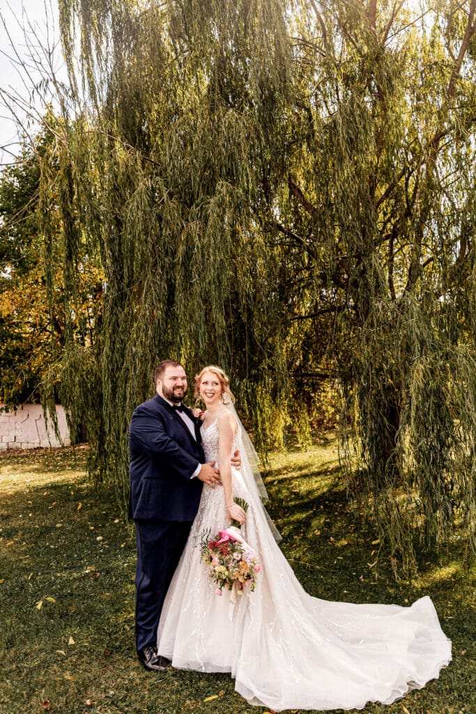 Bride and groom standing together under willow tree during portraits