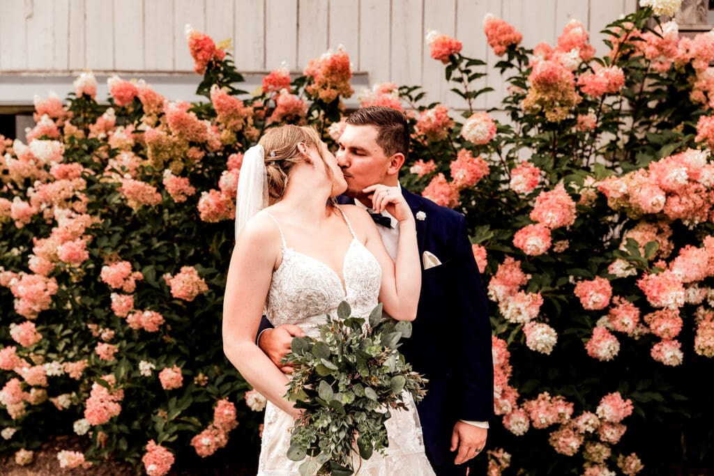 Bride and groom kissing in front of floral arrangements at The Barn at Ever Thine wedding in Butler County, Pennsylvania