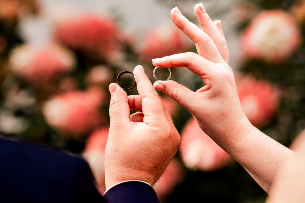 Close-up of bride and groom holding wedding bands in front of florals at The Barn at Ever Thine in Fenelton, PA