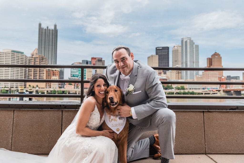 Wedding couple poses with their dog on a rooftop terrace with Pittsburgh skyline at Sheraton