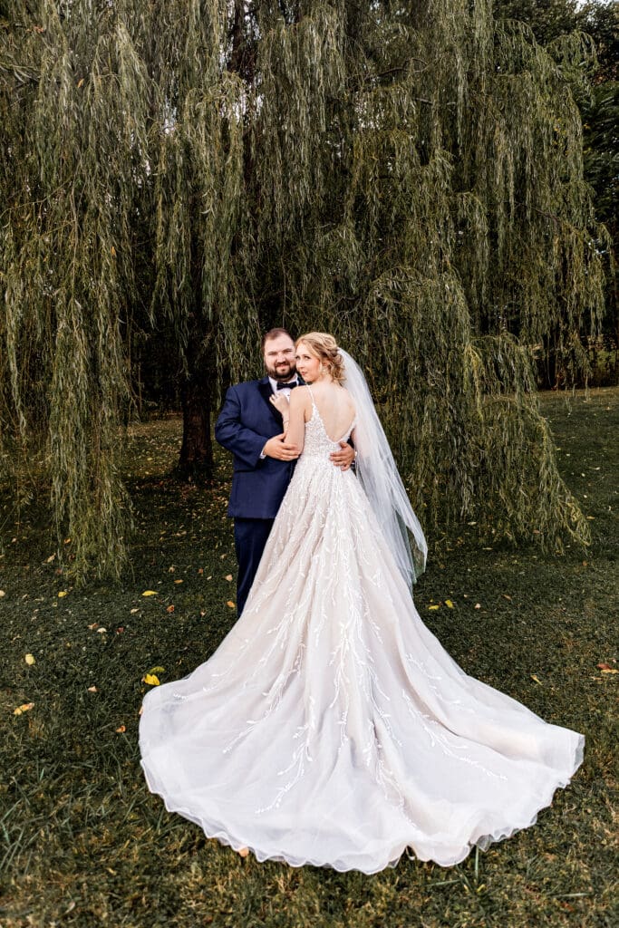 Bride and groom standing close together under willow tree during portraits at The Gathering Place at Darlington Lake