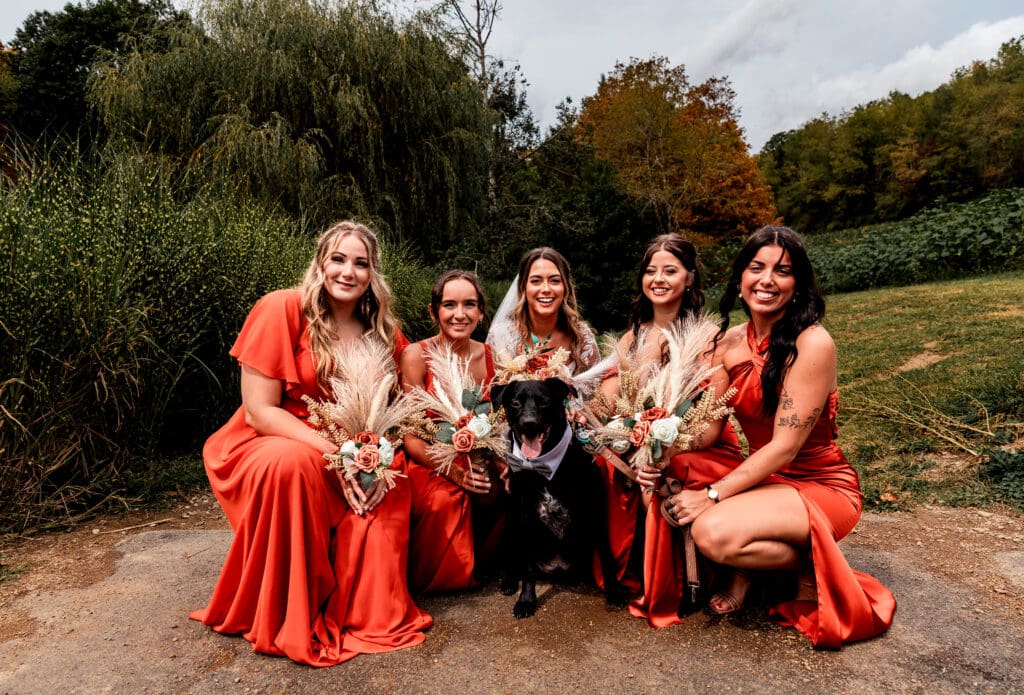 Bride and bridesmaid posing with couple’s dog at Hinckston Run Farm wedding