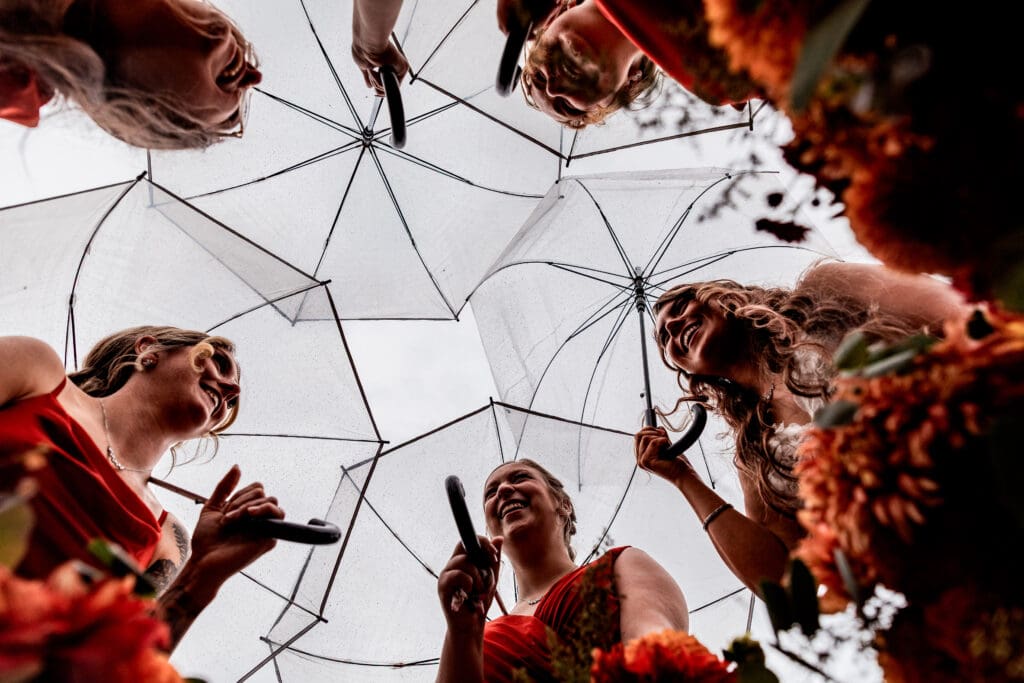 Bride and bridesmaids laugh beneath clear umbrellas at Hinckston Run Farm