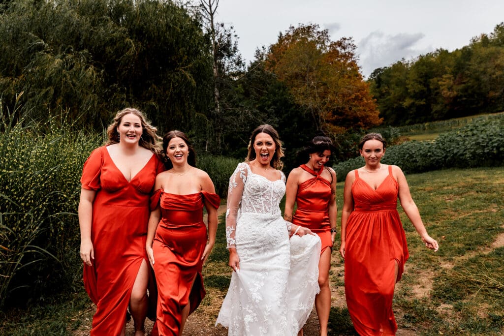 Wedding party in terracotta bridesmaid dresses and white wedding gown walking outdoors at Hinckston Run Farm