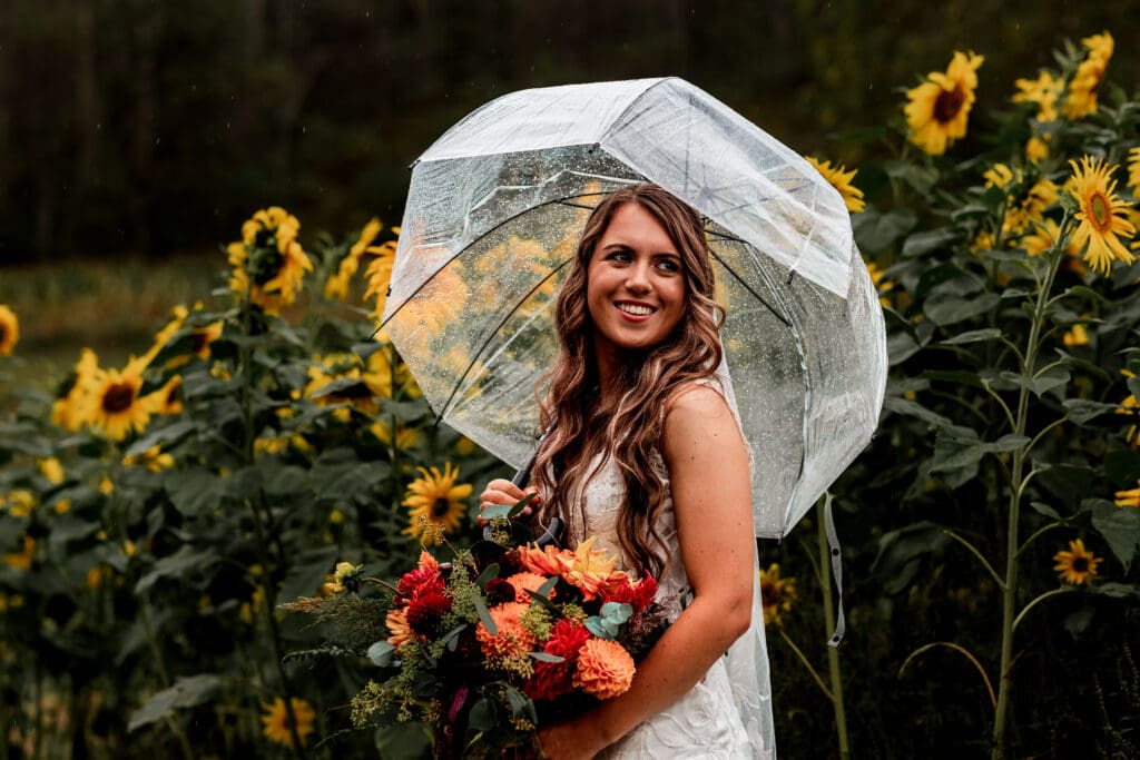 Bride holds bouquet and umbrella among sunflowers at Hinckston Run Farm