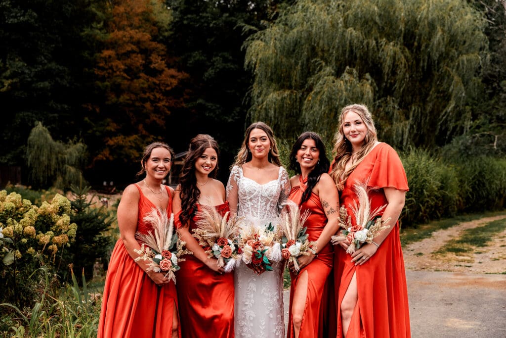 Wedding party in terracotta bridesmaid dresses and wedding dress posing outdoors with willow trees and autumn foliage at Hinckston Run Farm