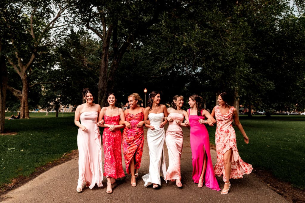 Bridesmaids in shades of pink dresses walking arm in arm with bride at the National Aviary