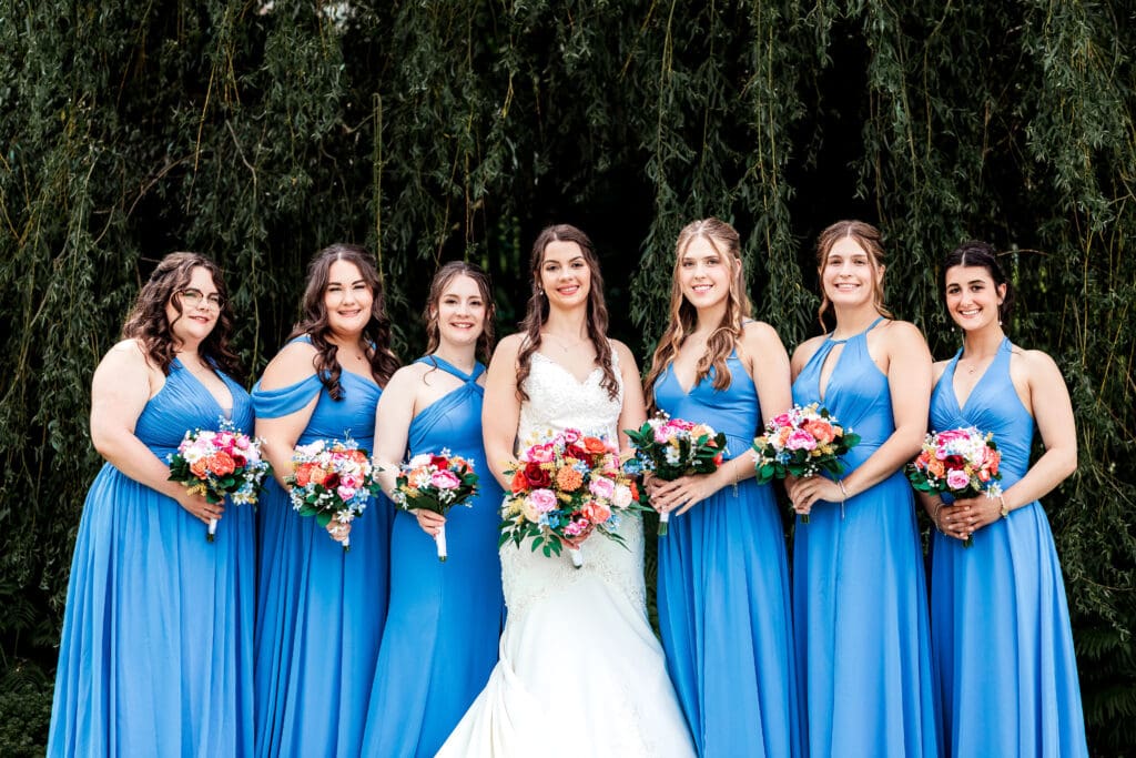 Bridesmaids in blue dresses hold coral and pink bouquets at Willowbrook