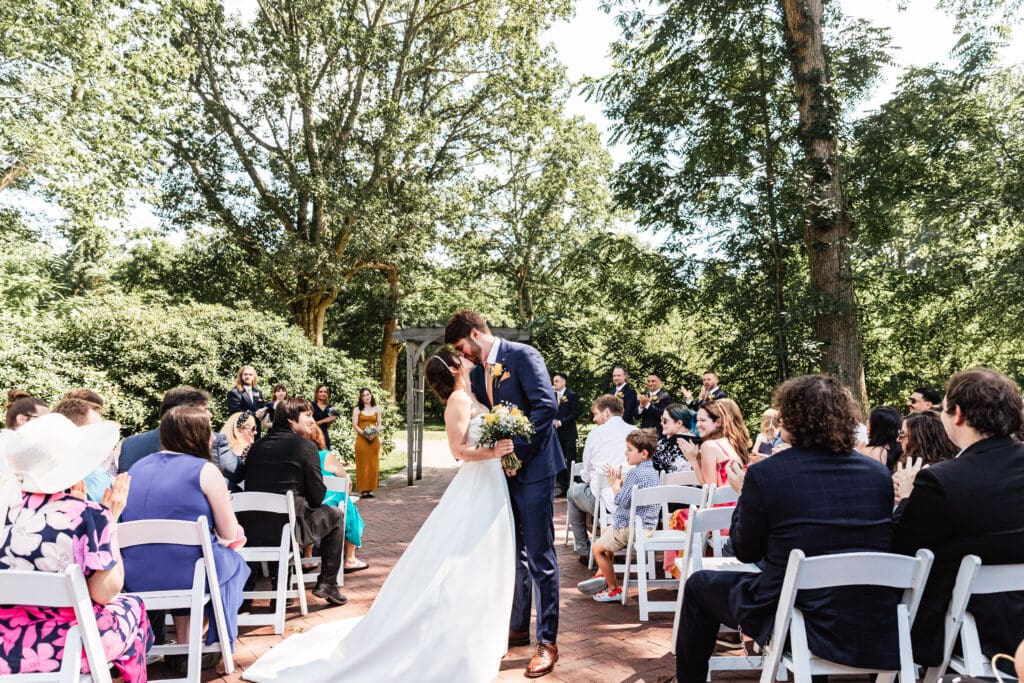Bride and groom sharing mid-aisle kiss during wedding ceremony at Succop Nature Park