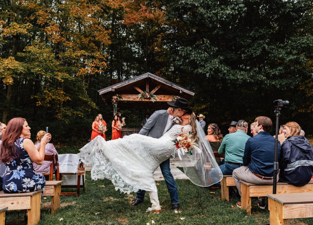 Wedding couple sharing dip kiss during outdoor fall ceremony at Hinckston Run Farm