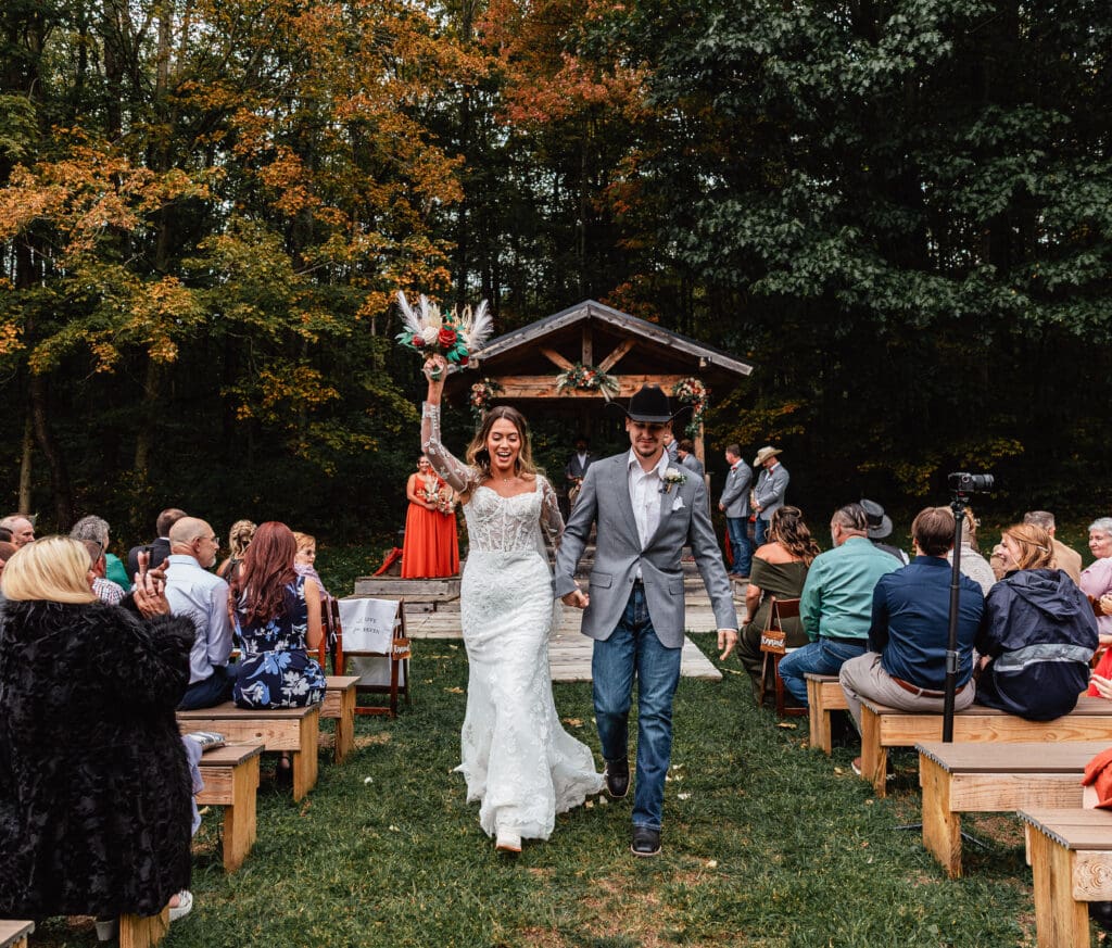 Newly pronounced husband and wife celebrating and walking down the ceremony aisle together at Hinckston Run Farm