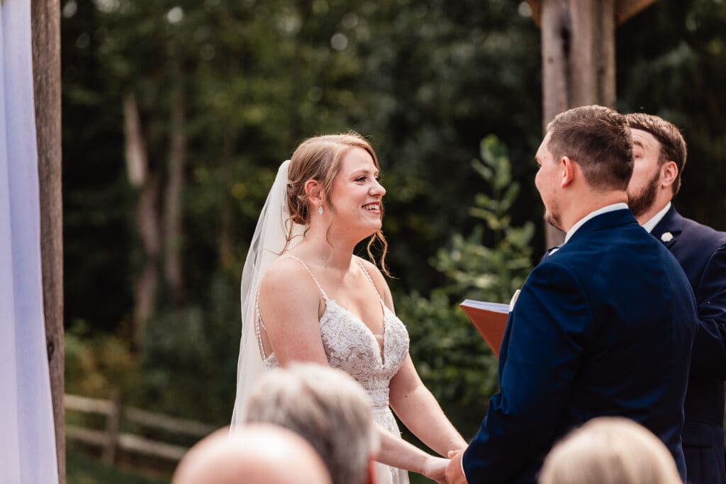 Bride smiling lovingly at her groom during their ceremony at The Barn at Ever Thine in Butler County, Pennsylvania