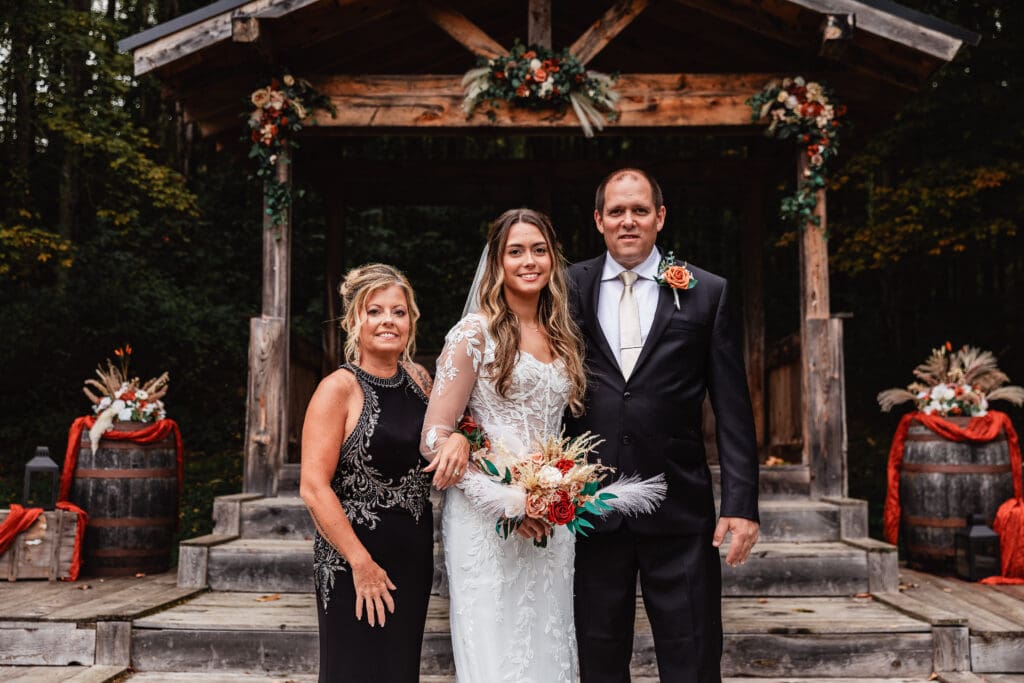 Bride posing with parents at rustic outdoor venue with wooden beams at Hinckston Run Farm