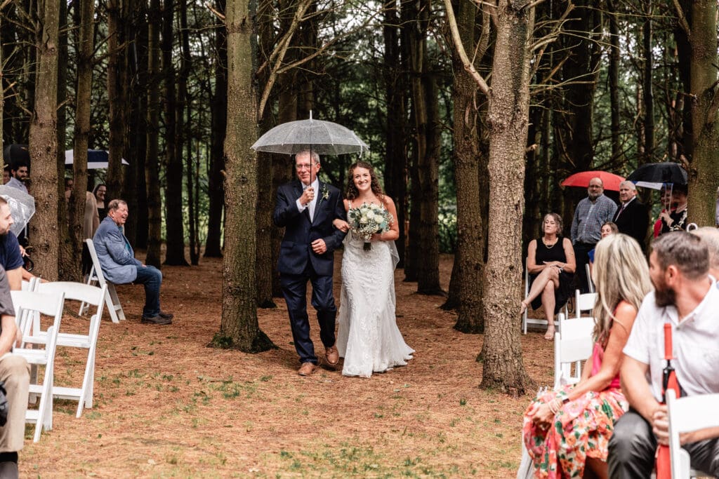 Bride escorted down the aisle under umbrellas by her father during a rainy Sanaview Farm wedding in Somerset, PA
