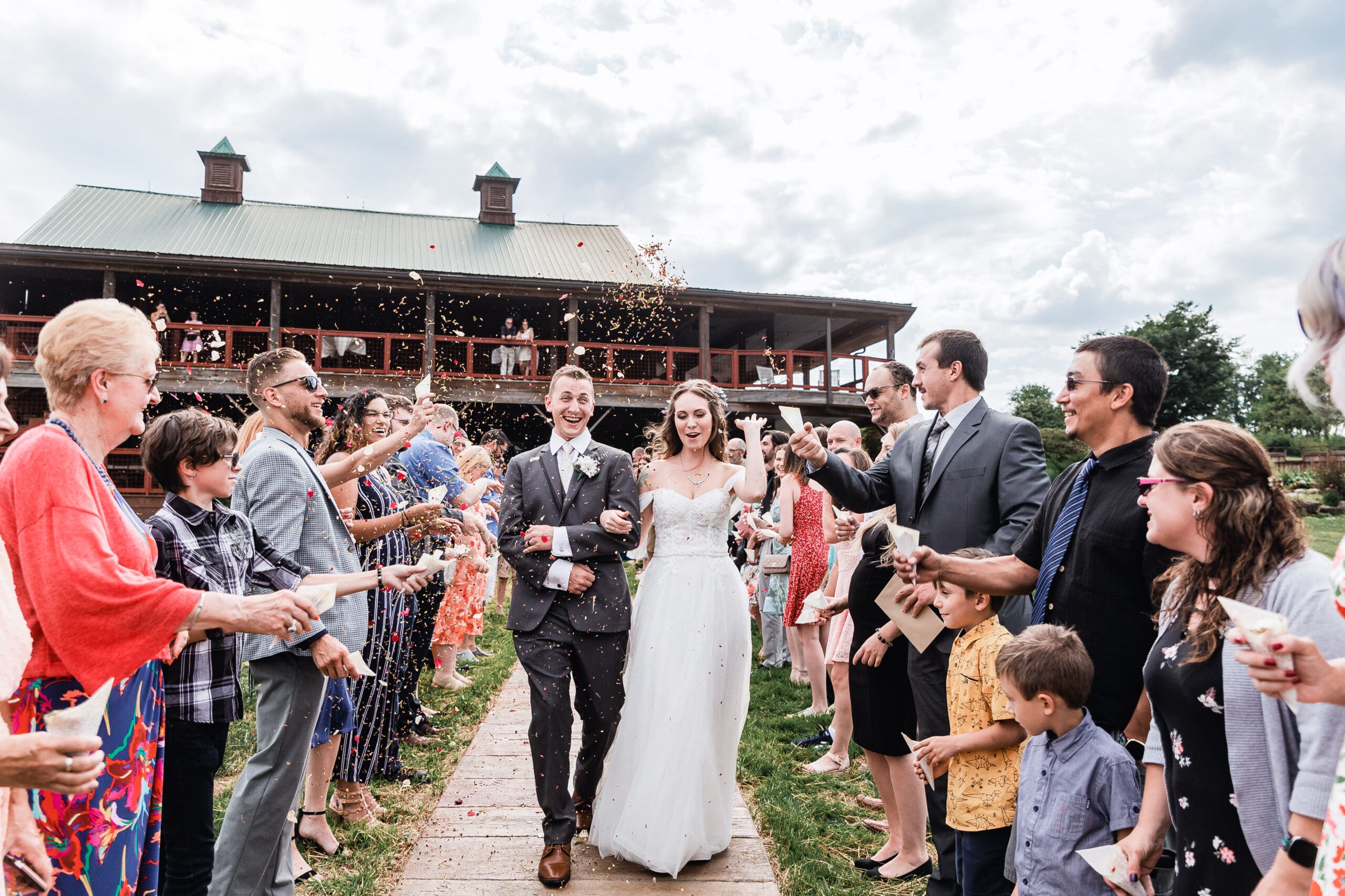 Wedding couple celebrates as flower petals are tossed while walking down the aisle at Lingrow Farm