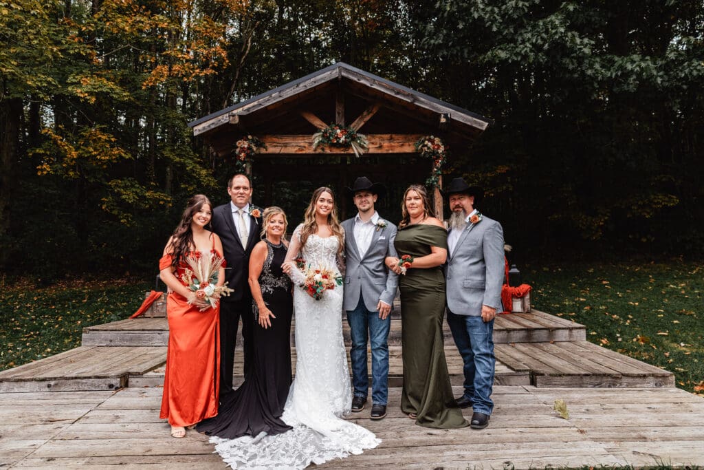 Wedding couple posing with both sides of family on rustic wooden deck with fall foliage at Hinckston Run Farm