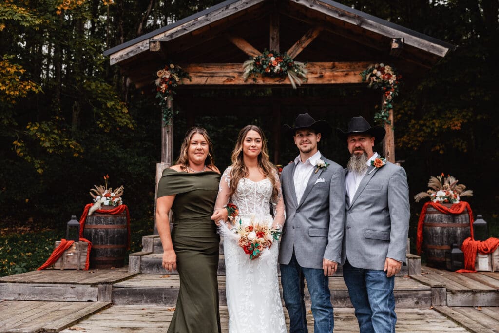 Wedding couple posing with parents at rustic outdoor venue with wooden beams at Hinckston Run Farm