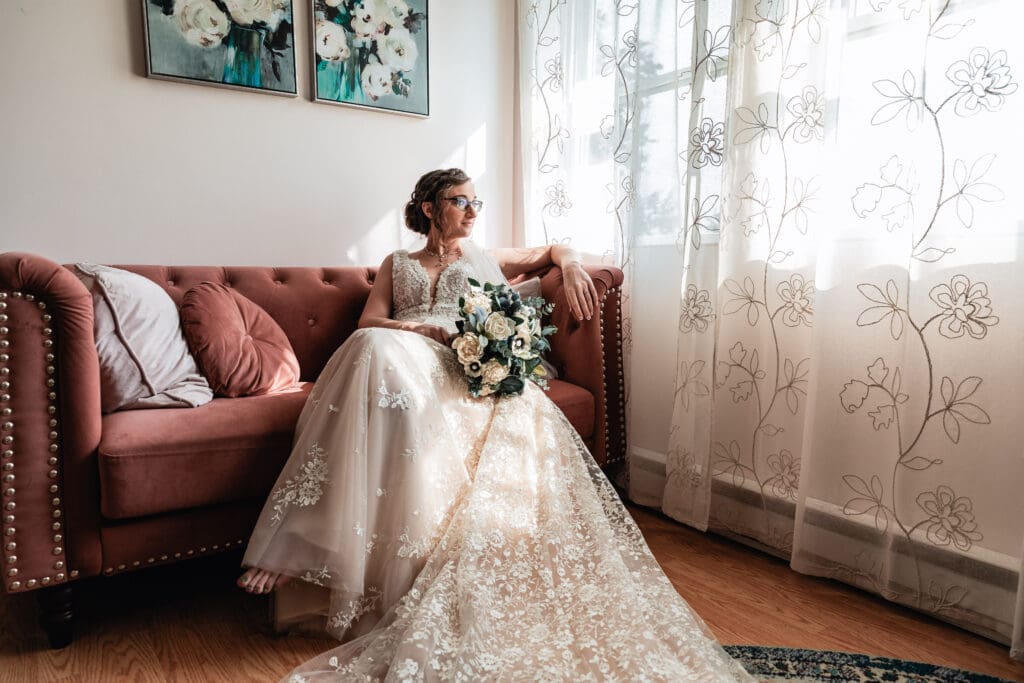 Bride relaxing on pink couch and gazing out of window in Pinehall at Eisler Farm bridal suite