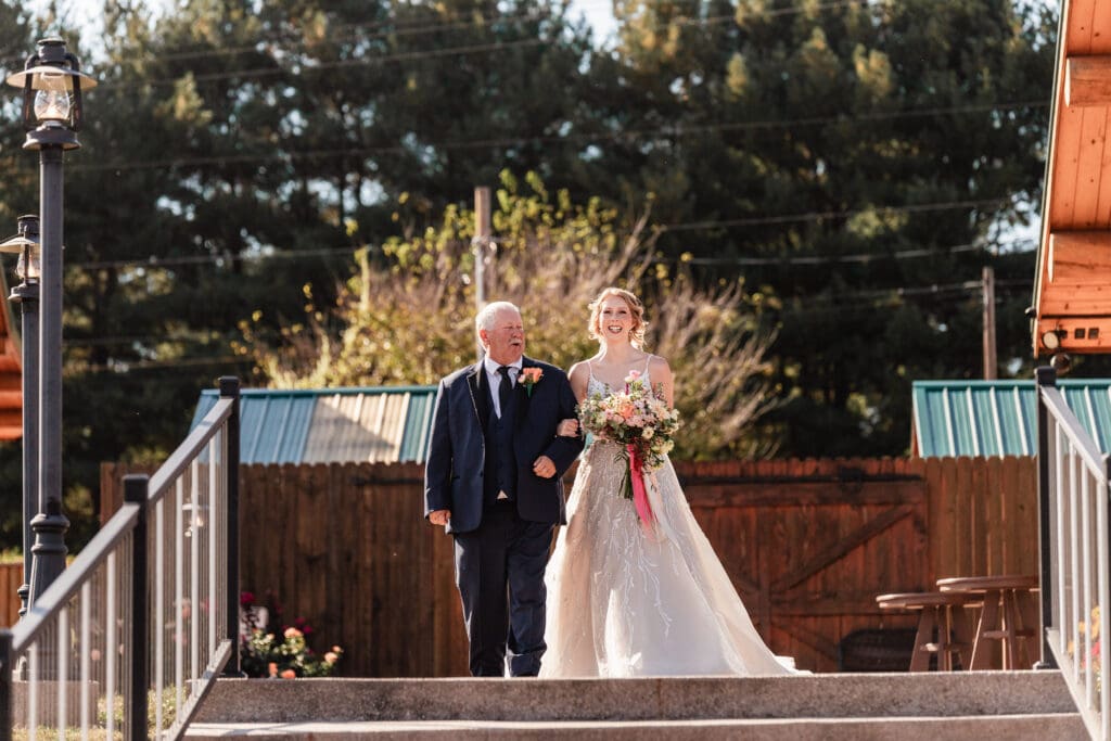 Bride holding her father’s arm as they walk down the aisle at The Gathering Place at Darlington Lake