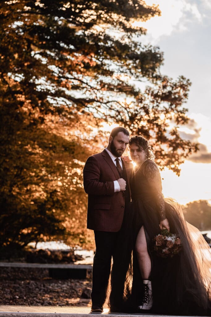 Gothic wedding couple poses on a dock at sunset wearing black wedding attire at Deep Creek