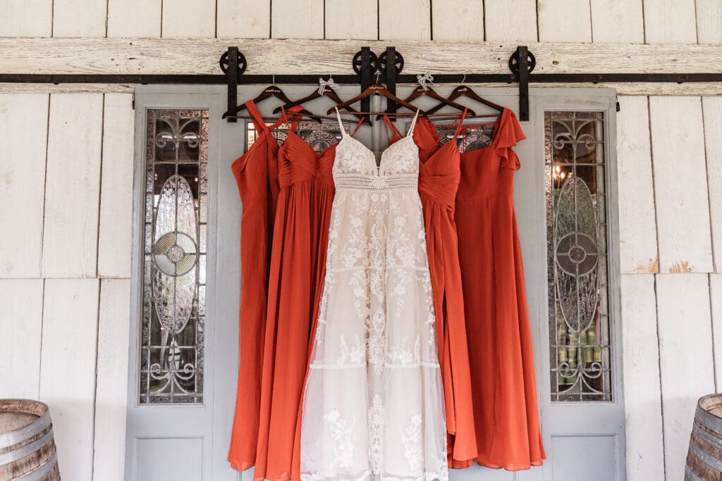 Bride and bridesmaids’ dresses hanging on a sliding blue stained-glass barn door at The Barn at Ever Thine in Fenelton, Pennsylvania
