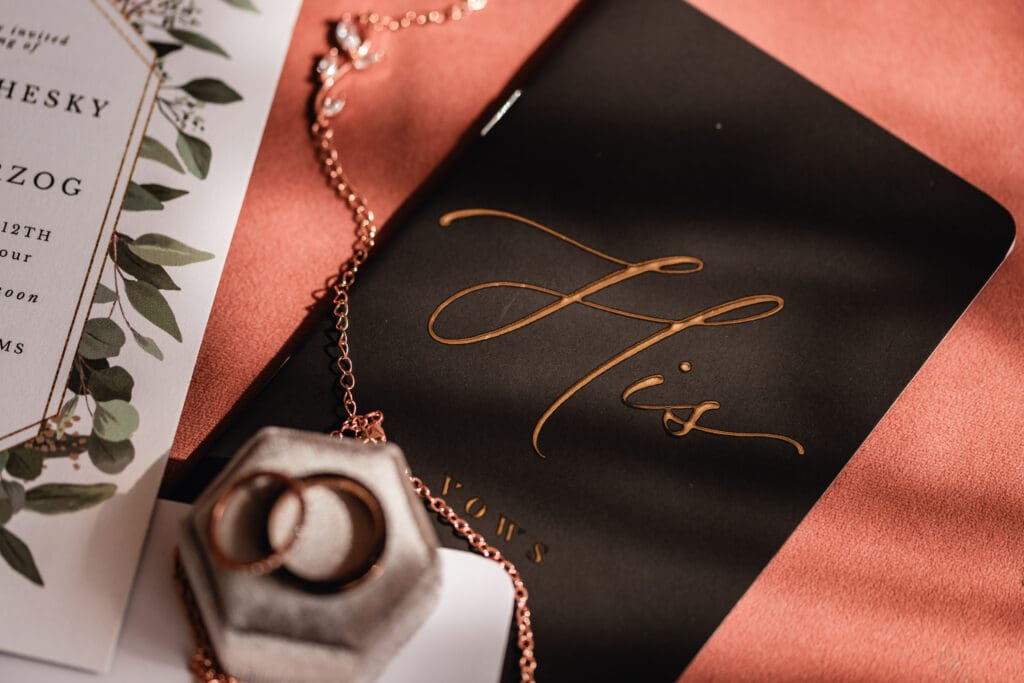 Detail photo of groom’s vow book surrounded by wedding invitations and rings at Pinehall at Eisler Farm