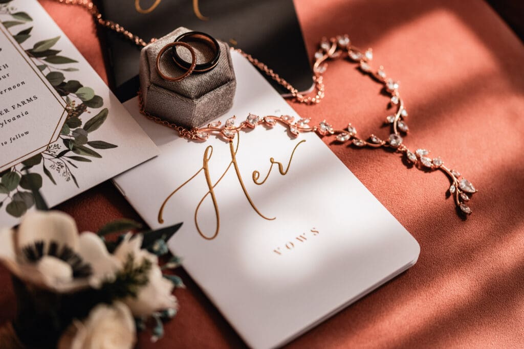 Detailed photo of bride and groom’s vow book with wedding bands, necklace, and sola flowers at Pinehall at Eisler Farm