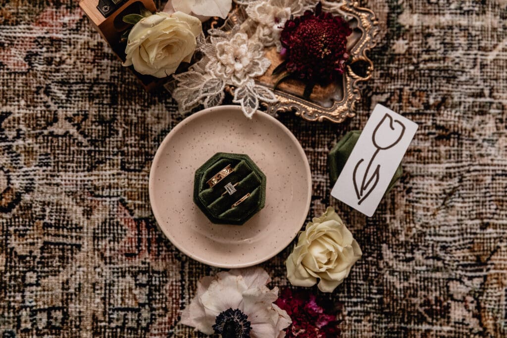 Flat lay of embroidered bridal lace, purple and cream flowers, gold tray, and wedding rings styled for a Lingrow Farm wedding