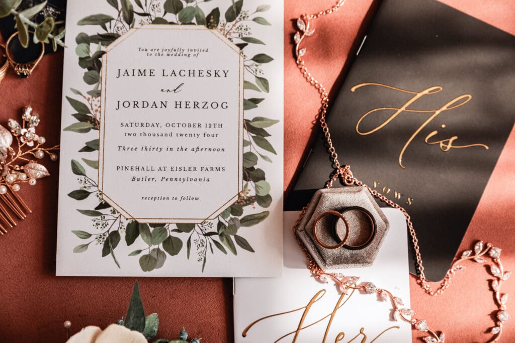 Bride and groom’s vow book surrounded by wedding bands, invitations, necklace, and sola flowers at Pinehall at Eisler Farm
