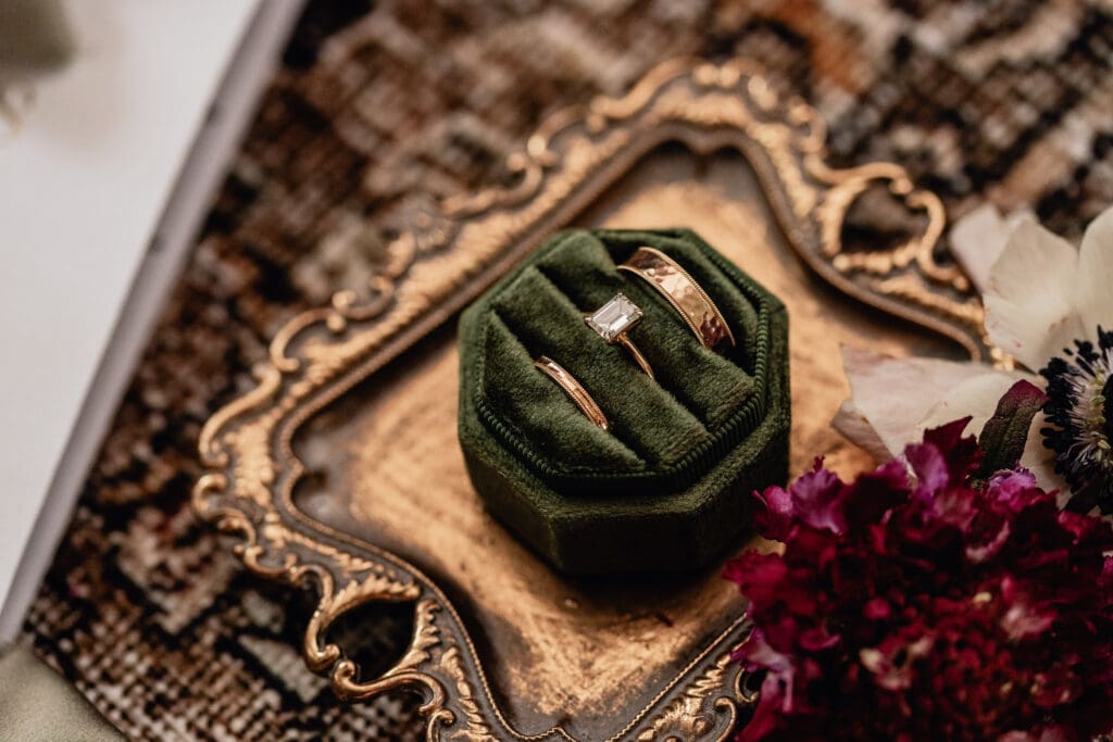 Green velvet ring box with wedding bands styled on a vintage gold tray with floral accents at a Lingrow Farm wedding