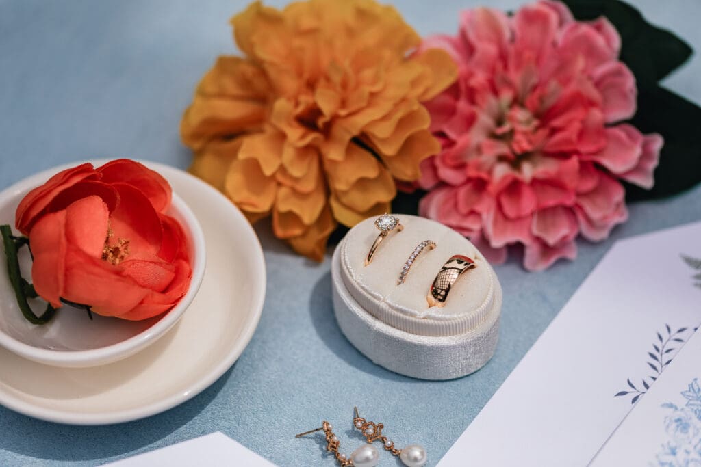 Wedding rings displayed beside pink and orange flowers in a styled flat lay