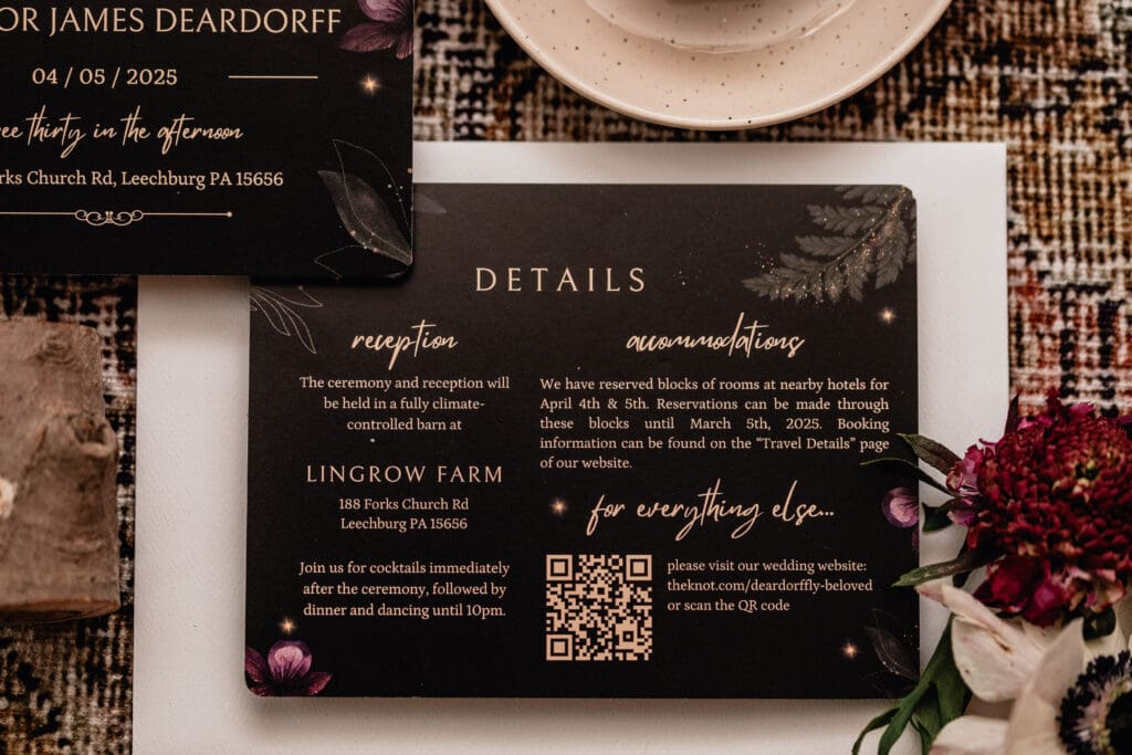 Flat lay of elegant black wedding details card with gold script, QR code, floral accents, and rustic vintage decor at Lingrow Farm