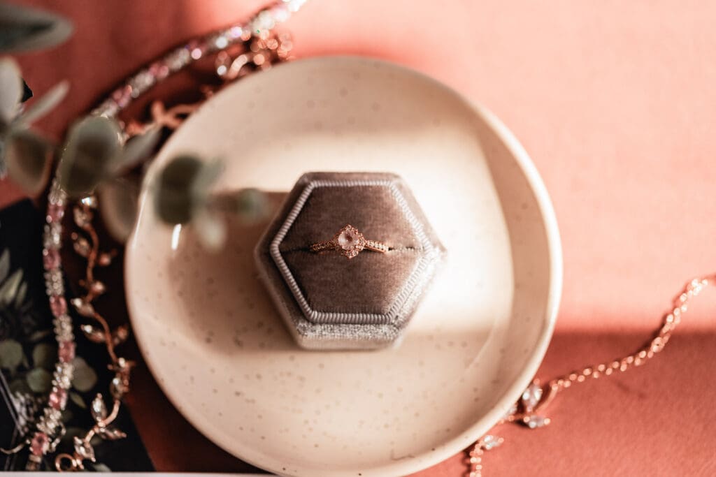 Close-up of bride’s engagement ring in silver ring box on cream circular ring dish at Pinehall at Eisler Farm