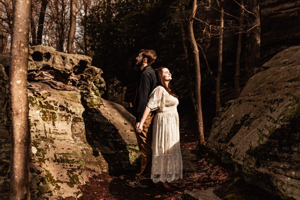 Engaged couple leaning back to back while enjoying a break in the clouds at Coopers Rock State Park