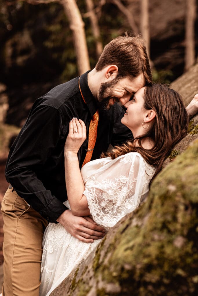 Engaged couple resting foreheads together while leaning against a rock at Coopers Rock State Park