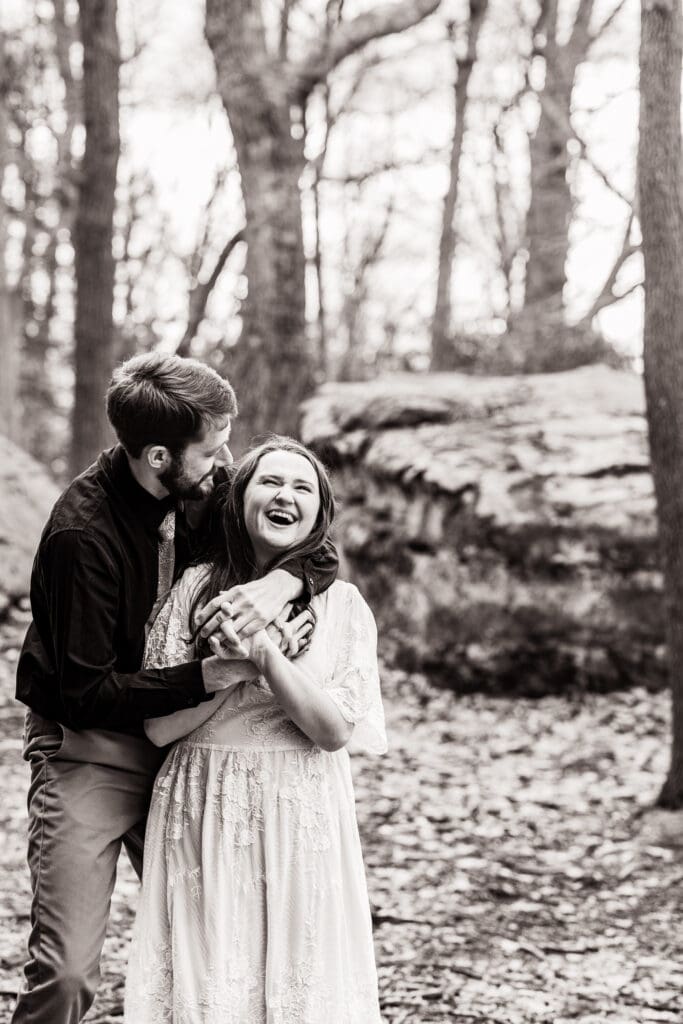 Black and white photo of a groom hugging his laughing fiancée during a Coopers Rock engagement session