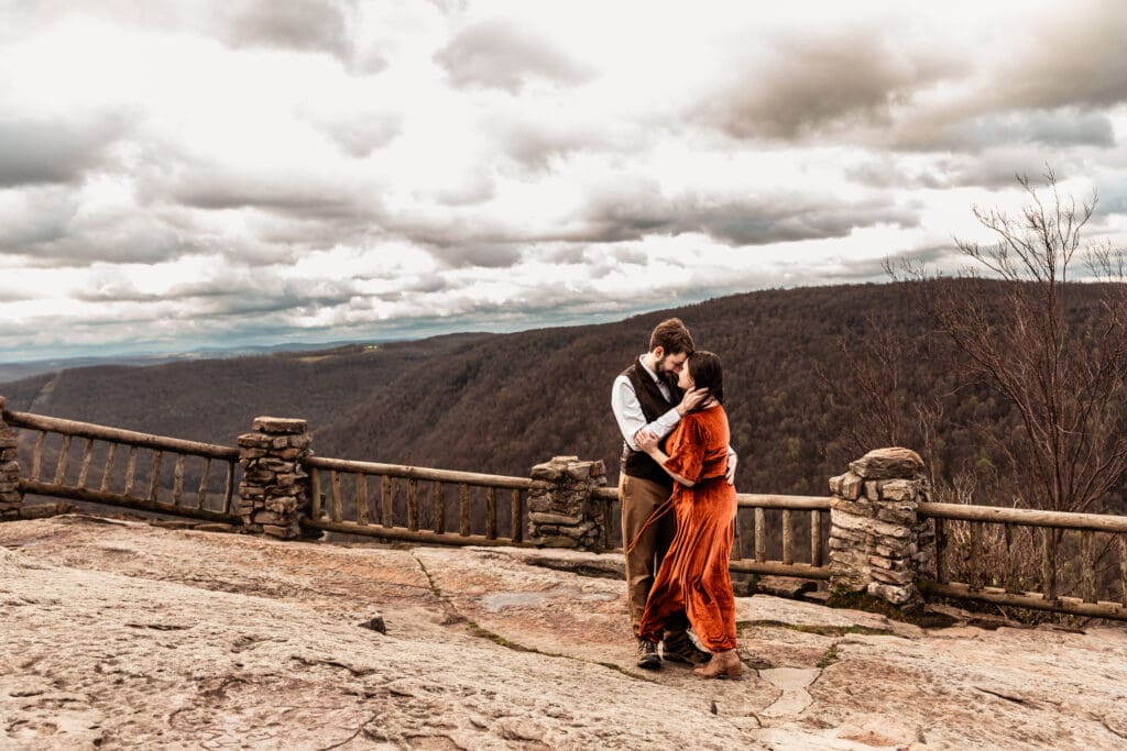 Couple hugging on the Coopers Rock overlook as wind blows through their hair during an engagement session
