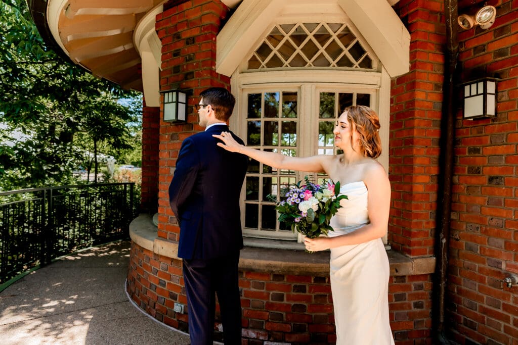 Bride tapping her groom on the shoulder during their first look at Schenley Park Welcome Center