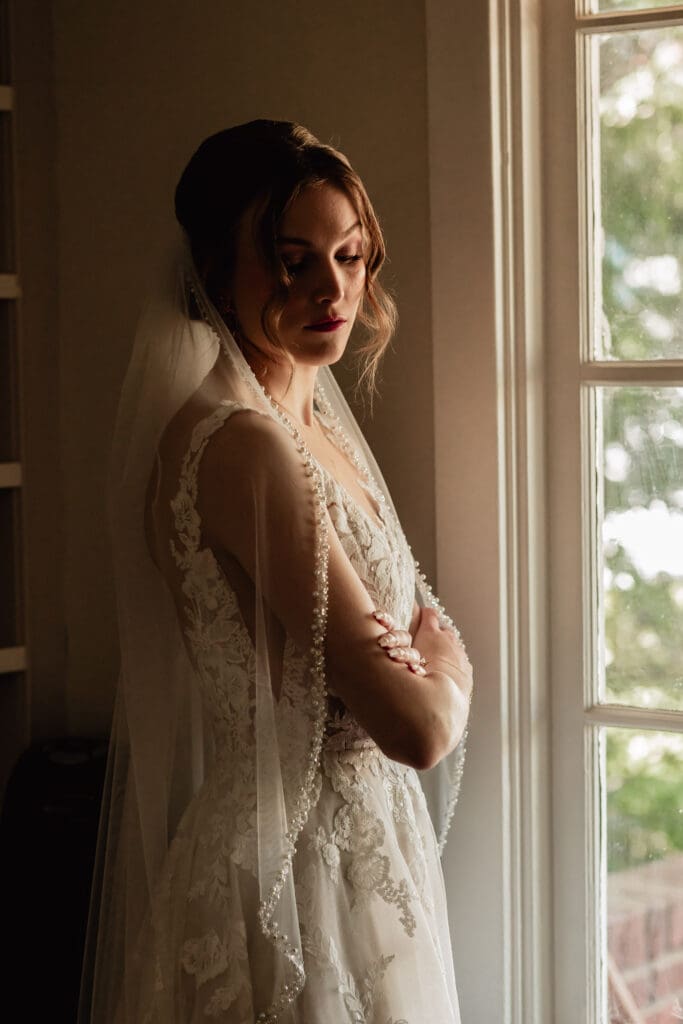 Bride standing with arms crossed, illuminated by window light before her Phipps Botanical Gardens wedding in Pittsburgh