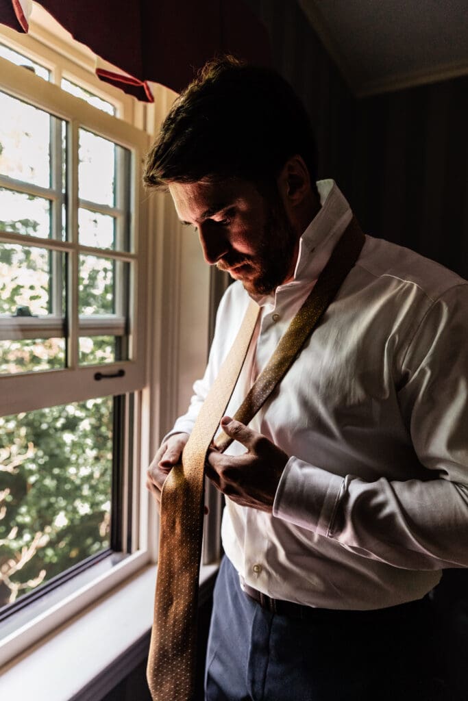 Groom adjusting tie and laughing with tie draped around neck with groomsmen at Succop Nature Park