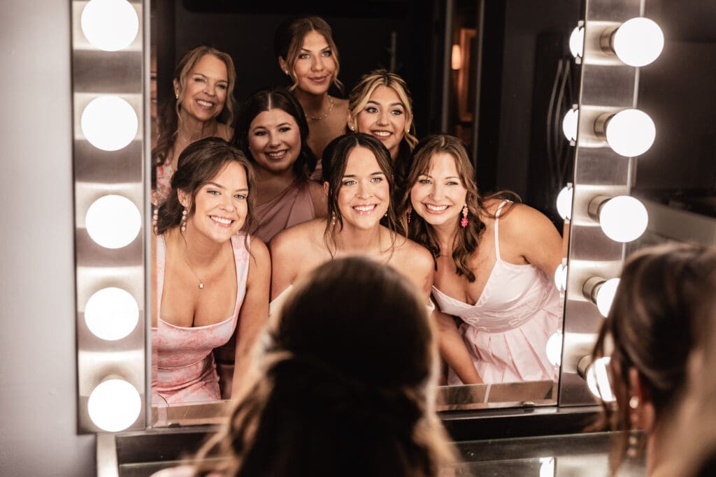 Bride and bridesmaids smiling at their reflection in a Hollywood vanity mirror at Willowbrook in Volant, Pennsylvania