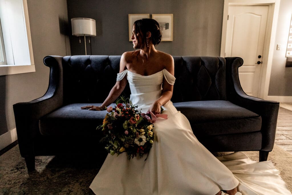 Pittsburgh bride sitting on a velvet blue couch and gazing out the window of the Willowbrook bridal suite in Volant, PA