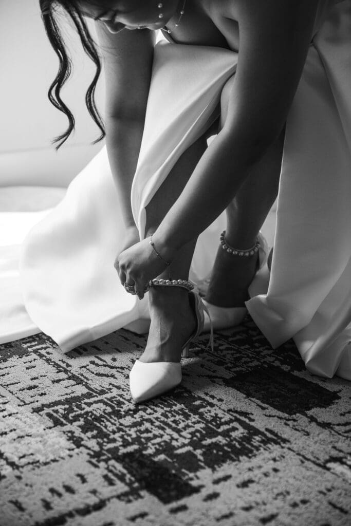 Black and white photo of bride fixing shoe strap at Sheraton Station Square