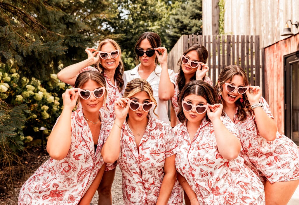 Bride and bridesmaids wearing heart-shaped sunglasses and posing playfully at Willowbrook wedding in Volant, Pennsylvania