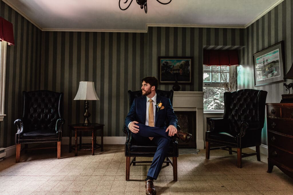 Groom sitting in middle of elegant room during wedding prep at Succop Nature Park